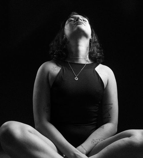 Person meditating with a calm expression, sitting cross-legged in a minimalist setting.